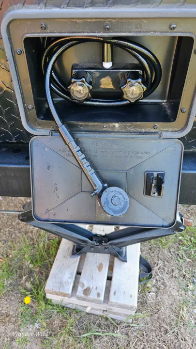 Outdoor RV rental shower unit, with hose, showerhead, water knobs, and winterizing instructions on the open lid.. Forest River Viking 2018
