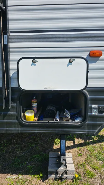 RV rental's open storage with camping gear, a leveling jack, and wood blocks for stability.. Forest River Viking 2018