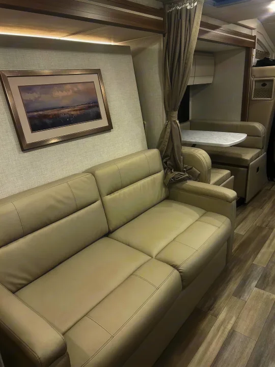 Modern rv rental interior: light sofa, framed art, and dining area with curtain. Neutral tones, wood-look floor.. Thor Delano 2026