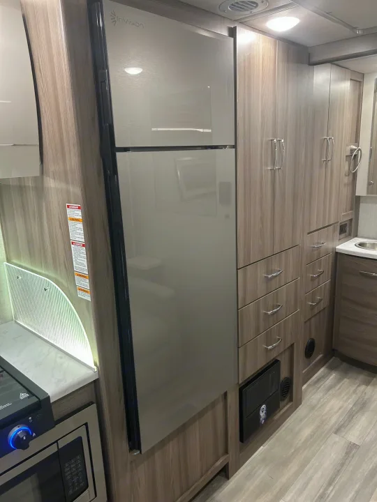 RV rental kitchen area: stainless refrigerator, wood cabinetry, countertop, microwave, and sink. Functional and modern interior.. Thor Delano 2026