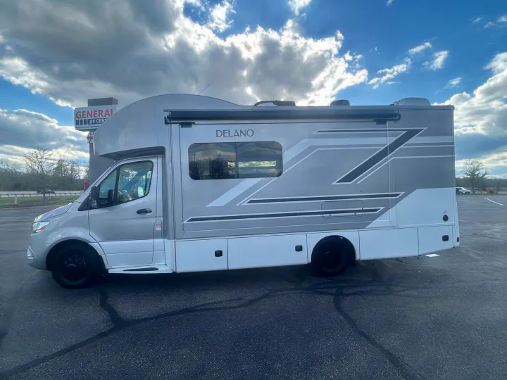 Modern DELANO RV rental, a sleek motorhome with an awning, parked at a dealership under a dynamic sky. Perfect for travel!. Thor Delano 2026