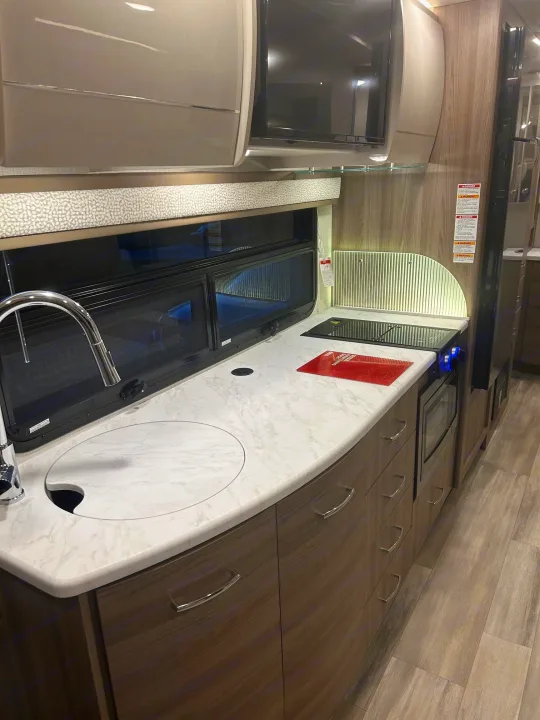 Modern RV rental kitchen featuring a sleek countertop, sink, stovetop, microwave, and storage cabinets.. Thor Delano 2026