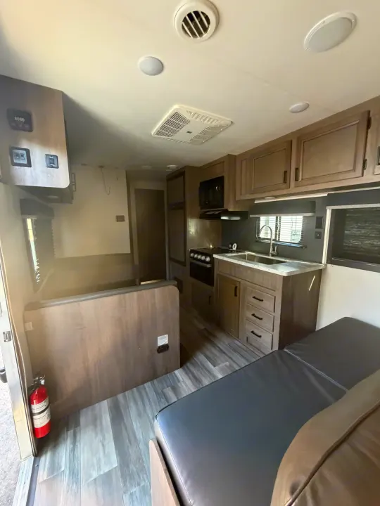 RV rental interior featuring a modern kitchen with stove, sink, microwave, dinette, and bed. Wood-look flooring & cabinets.. Starcraft Autumn Ridge 2022