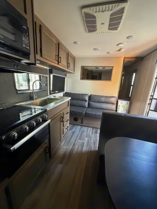 This RV rental features a modern interior with a kitchen (stove, sink, microwave) and living space (sofa, dining table). Light wood and grey tones.. Starcraft Autumn Ridge 2022