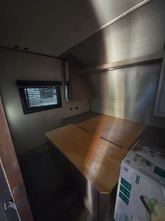 Interior of an RV rental bedroom featuring a wooden bed base, window with blinds, overhead light, and a new mattress in a box.. Starcraft Autumn Ridge 2022