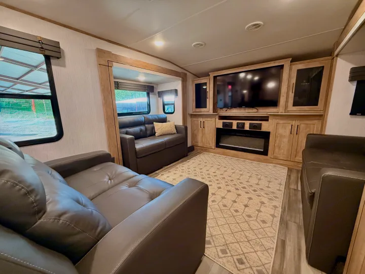Spacious RV rental living area featuring two gray sofas, a large TV, electric fireplace, and cozy rug, perfect for relaxation.. Heartland RVs Milestone 2023