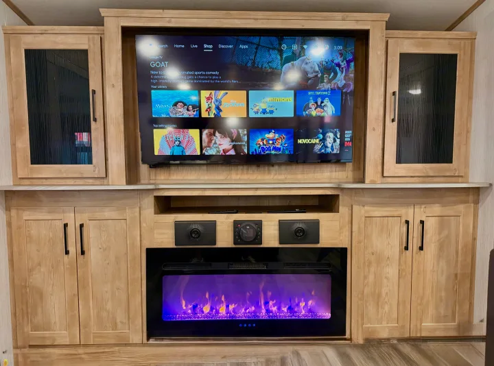 RV rental entertainment center featuring a large TV with Google TV interface, a purple-lit electric fireplace, and integrated speakers.. Heartland RVs Milestone 2023