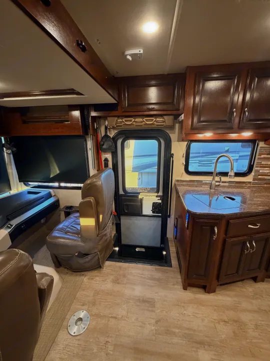 Spacious rv rental interior featuring a kitchen with sink, dark wood cabinets, and comfortable brown captain's chairs.. Fleetwood Bounder 2018