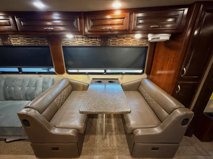 RV rental dinette: brown benches, speckled table, dark cabinets, valances, & ambient lighting.. Fleetwood Bounder 2018