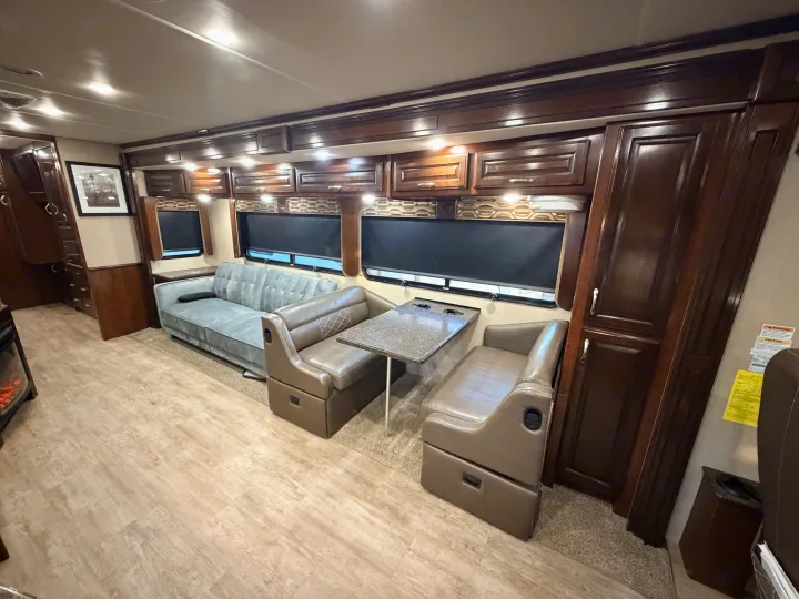 RV rental living area with a comfy sofa, dinette, and rich wood cabinetry. Bright interior, ready for your road trip.. Fleetwood Bounder 2018