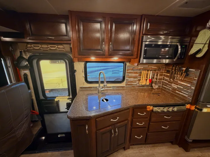 This rv rental features a well-appointed kitchen with dark wood cabinets, a sink, stovetop, microwave, and tiled backsplash.. Fleetwood Bounder 2018
