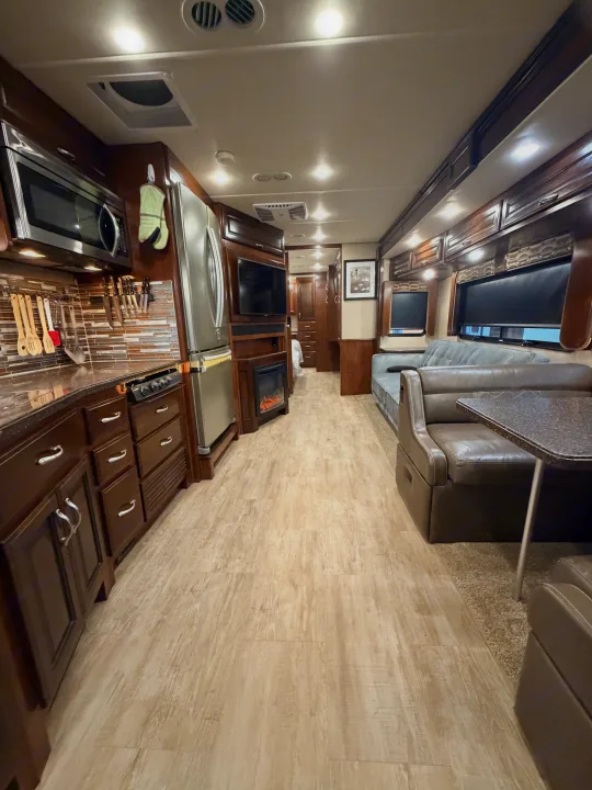Inside an RV rental: full kitchen, cozy living area with sofa & dining booth, fireplace, and light wood-look flooring.. Fleetwood Bounder 2018