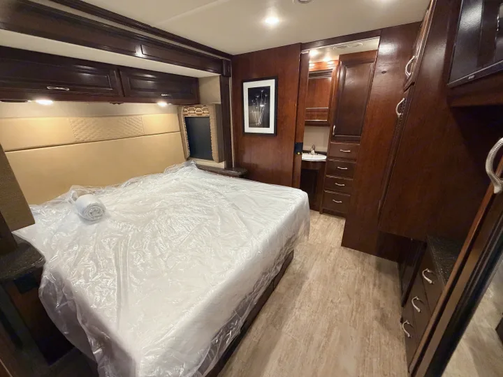 RV rental bedroom: a fresh, protected bed, dark wood storage cabinets, and a handy vanity with sink. Ready for your adventure.. Fleetwood Bounder 2018