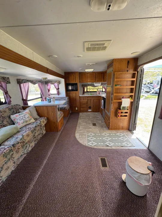 RV rental's inviting interior: floral sofa, dinette with purple curtains, and a well-equipped kitchen area.. Forest River Wildwood 2000