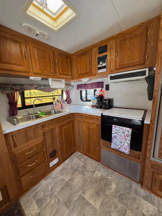 RV rental kitchen featuring warm wooden cabinets, a double sink, stove, and an overhead skylight.. Forest River Wildwood 2000