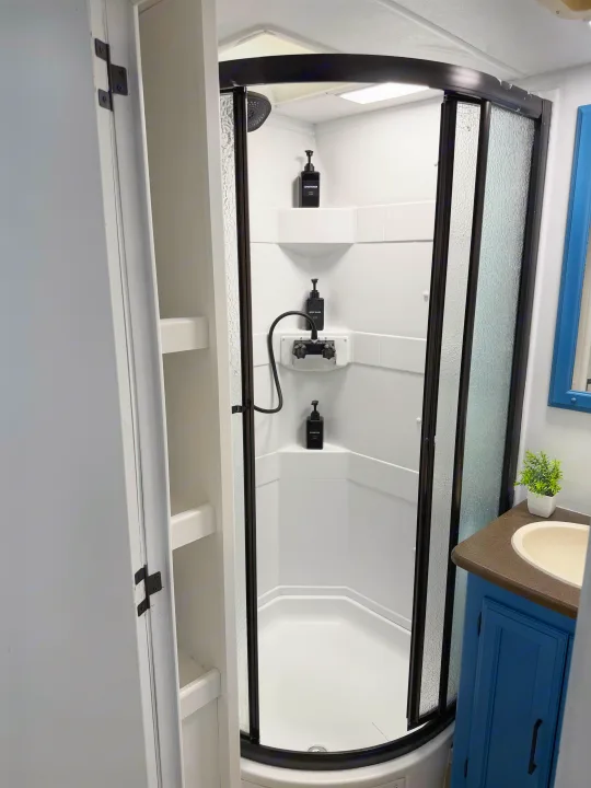 Clean RV rental bathroom featuring a modern corner shower, sink vanity with a blue cabinet, and open storage shelves.. Forest River Coachmen 2012