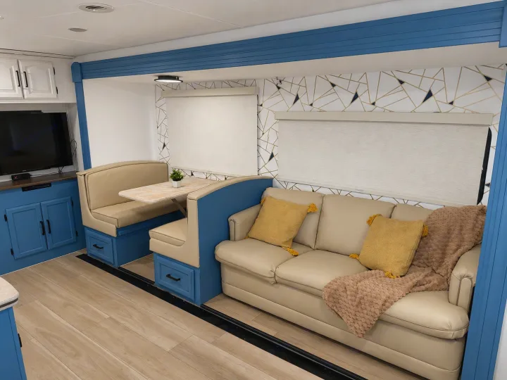 Spacious rv rental interior showing a blue-accented dining booth, beige sofa, and TV. Modern, comfortable living space.. Forest River Coachmen 2012