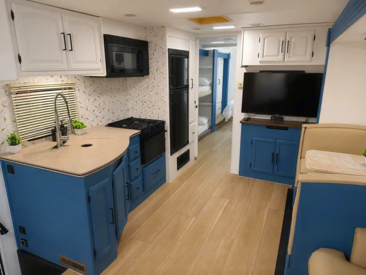This modern RV rental features a stylish blue kitchen, a comfy living area with a TV, and a peek into bunk beds.. Forest River Coachmen 2012