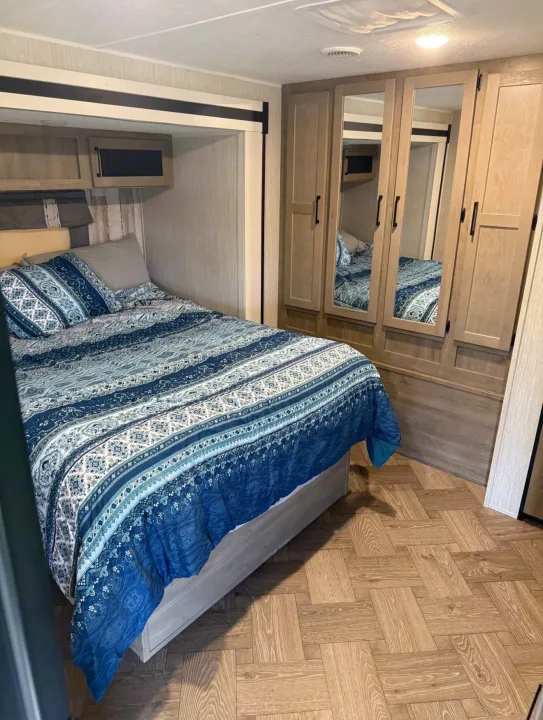 Inside a comfortable RV rental, featuring a bedroom with blue bedding, mirrored wardrobe, and wood floors. Perfect for road trips.. Forest River Palomino Puma 2022