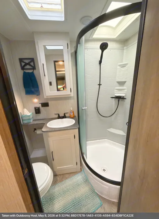 Compact RV rental bathroom featuring a corner shower, vanity with sink, and toilet, complete with a mirror and skylight.. Forest River Palomino Puma 2022