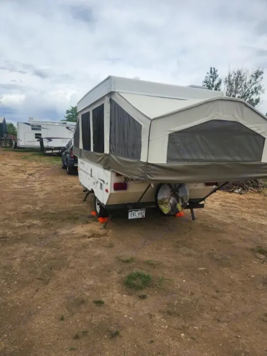 Explore the outdoors! This fully set up beige pop-up camper RV rental, seen from the rear, is parked with another RV in the background.. Forest River Rockwood Freedom 2009