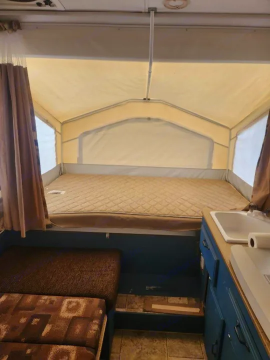 Cozy pop-up camper RV rental interior: bed, sink, and dining area. Ideal for camping adventures.. Forest River Rockwood Freedom 2009
