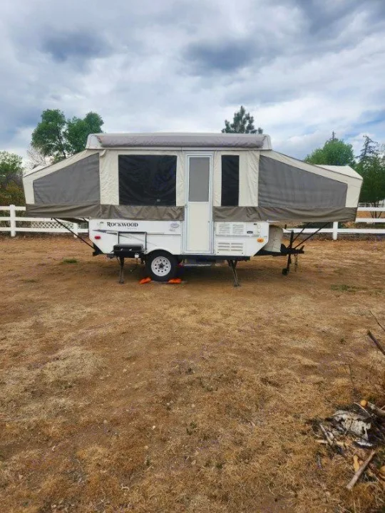 A Rockwood pop-up RV rental, fully expanded and set up on a dry field under cloudy skies, ready for your next camping trip.. Forest River Rockwood Freedom 2009