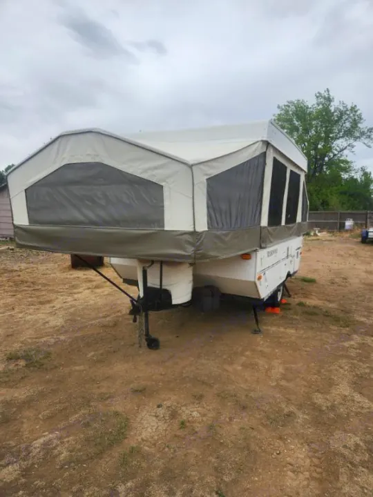 Pop-up camper RV rental, fully extended with tent sides, parked on a dirt lot under an overcast sky, ready for camping.. Forest River Rockwood Freedom 2009