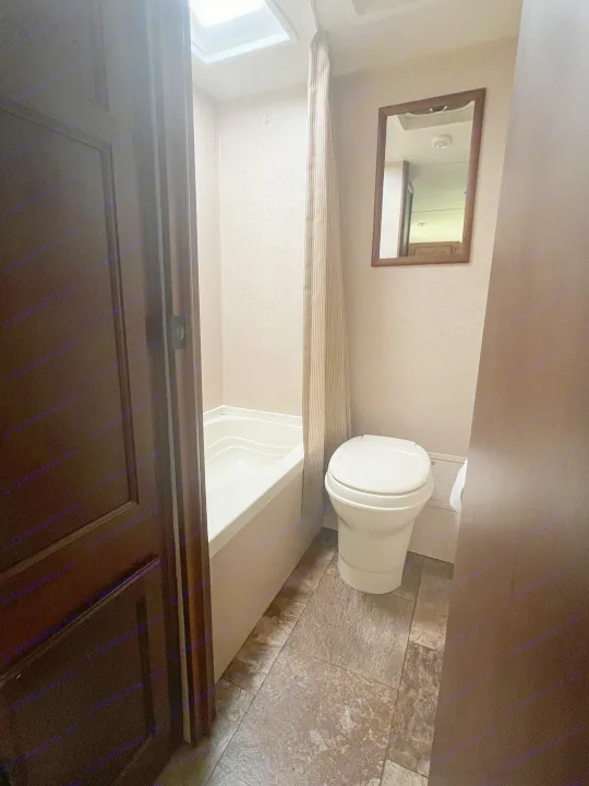 This RV rental bathroom features a small tub with a shower curtain, toilet, mirror, and tiled floor.. Jayco Jay Flight 2015
