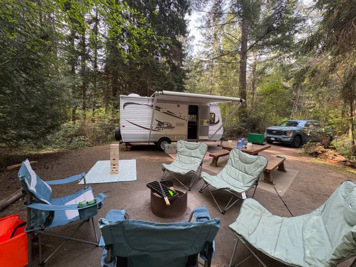 Relaxing at a forest campsite with an RV rental, chairs around a fire pit, and games. Perfect outdoor getaway.. Jayco Jay Flight 2015