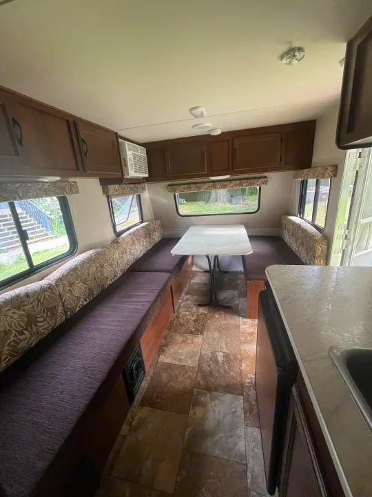 Bright rv rental interior featuring a cozy dinette with patterned cushions, overhead cabinets, and a partial kitchen counter.. Jayco Jay Flight 2015