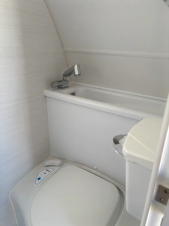 Compact bathroom in an RV rental, featuring a white toilet, integrated sink with chrome faucet, and small bin.. nuCamp T@B 2024