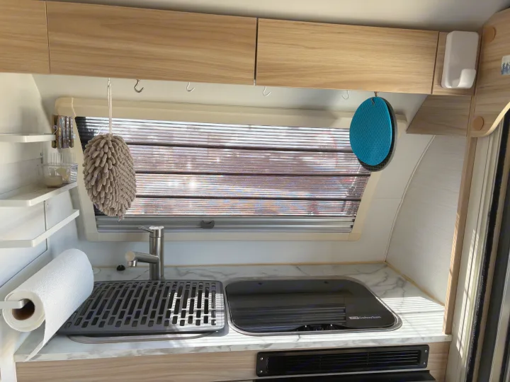 RV rental kitchen: functional space with sink, covered stove, window blinds, and overhead storage with hanging hooks.. nuCamp T@B 2024