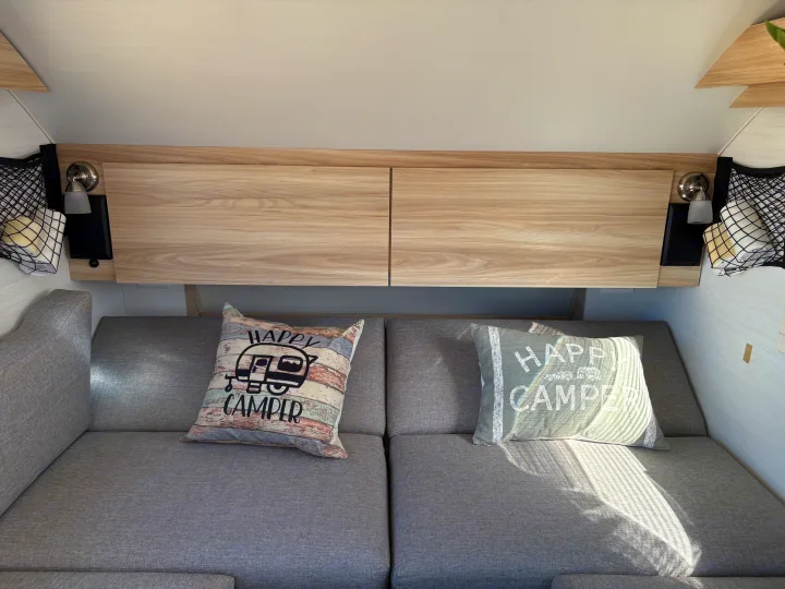 Cozy rv rental interior with grey seating, "Happy Camper" pillows, overhead storage, and reading lights.. nuCamp T@B 2024
