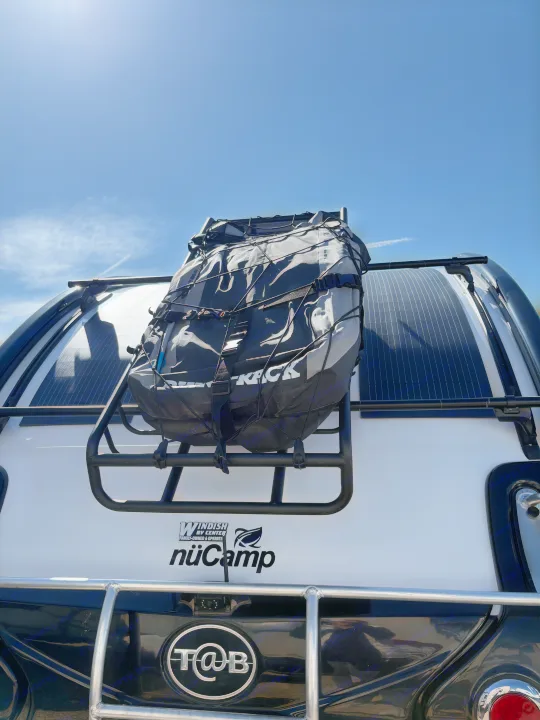 Back of a NuCamp T@B rv rental camper: cargo bag on a rack, solar panels on top, under a bright blue sky.. nuCamp T@B 2024
