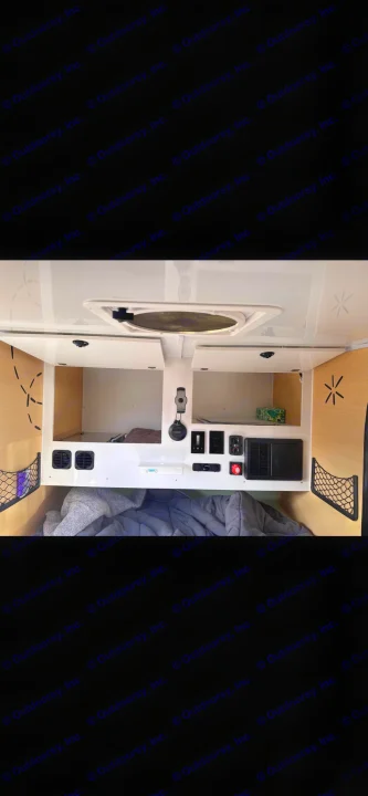 Inside a cozy RV rental: gray bedding, overhead storage, and a control panel with outlets. A compact camper interior for your trip.. Boreas MXT 2020