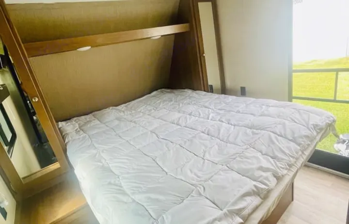 Cozy RV rental bedroom featuring a queen bed with a white comforter, overhead storage, and a bright window.. Aspen Trail Aspen Trail Trailer 2018