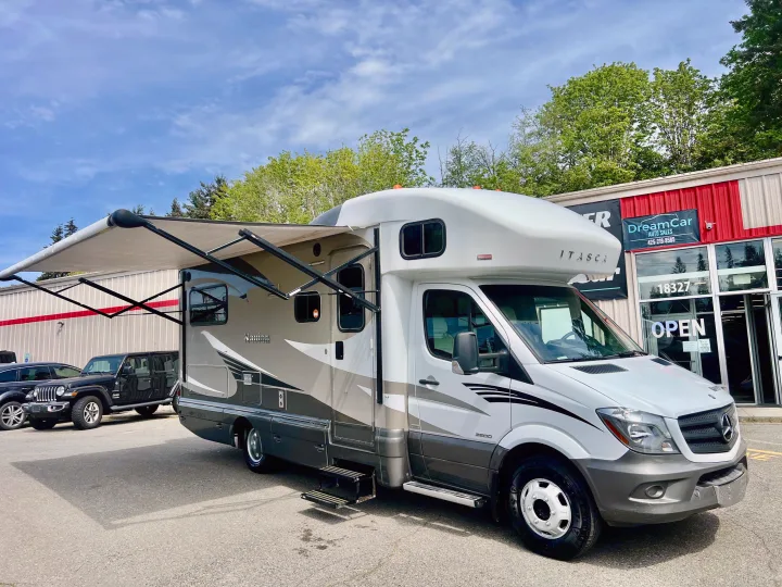 White & gray Itasca motorhome with its awning extended, parked at DreamCar Auto Sales for RV rental.. Itasca Navion 2014