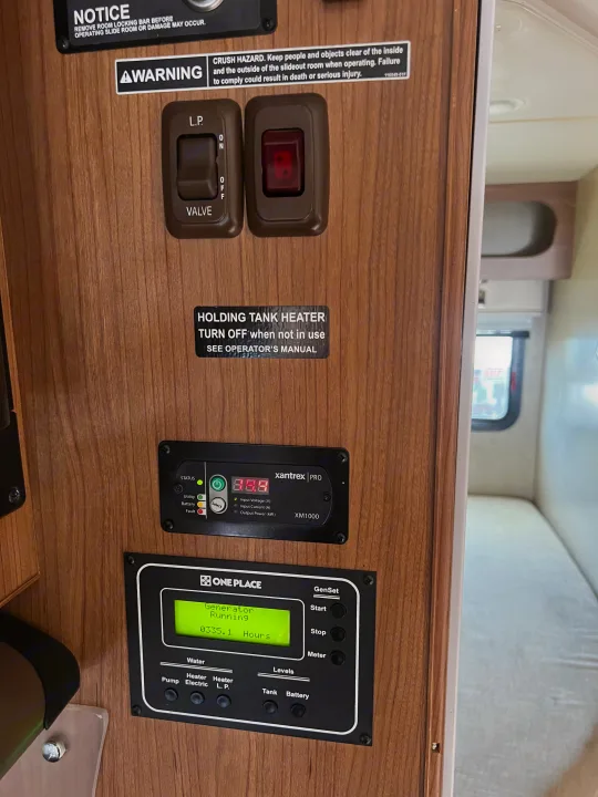 RV rental control panel: generator running (0335.1 hrs), water/tank heater controls, Xantrex inverter, safety alerts.. Itasca Navion 2014