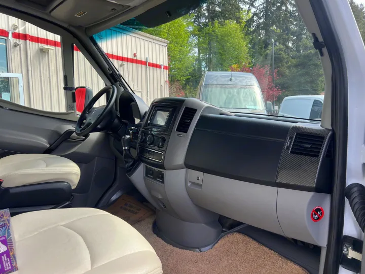 RV rental interior featuring cream seats, a modern dashboard with carbon fiber trim, and controls for "house power.". Itasca Navion 2014