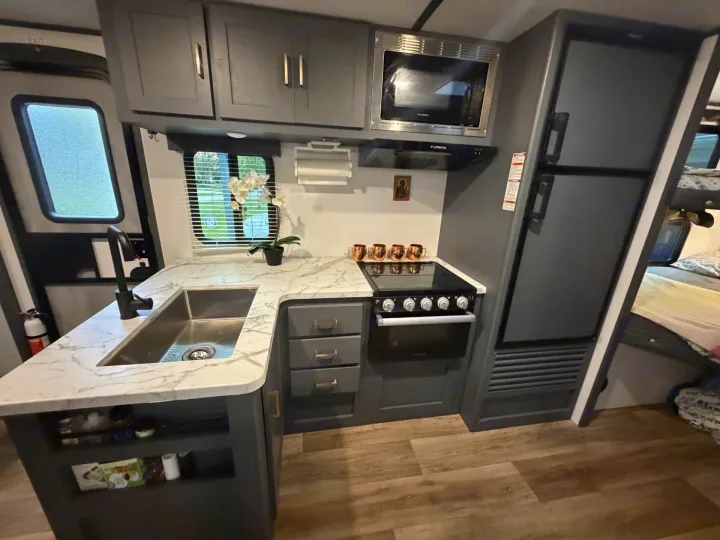 This modern RV rental kitchen features sleek dark cabinets, marble countertops, full appliances, and a spacious sink.. Keystone RV Bullet Crossfire 2022