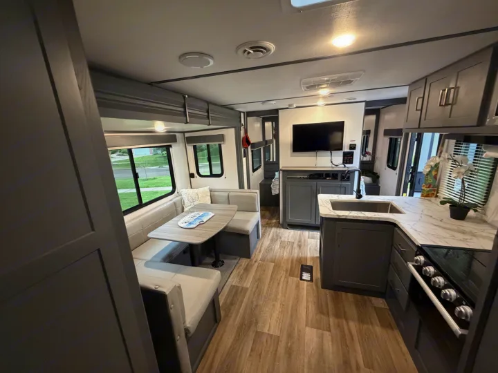 This modern rv rental interior features a spacious dinette, a full kitchen with dark cabinets, and a mounted TV.. Keystone RV Bullet Crossfire 2022
