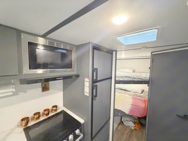 Modern gray rv rental interior: kitchen with microwave, stove, fridge, and cozy bunk beds for comfortable travel.. Keystone RV Bullet Crossfire 2022