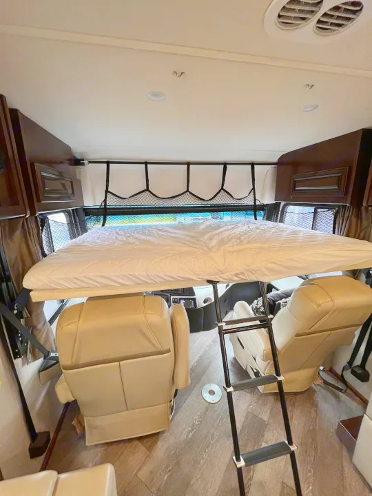 Inside an RV rental, a drop-down overhead bunk bed with a safety net and ladder maximizes sleeping space above the cockpit.. Fleetwood Pace Arrow 2020