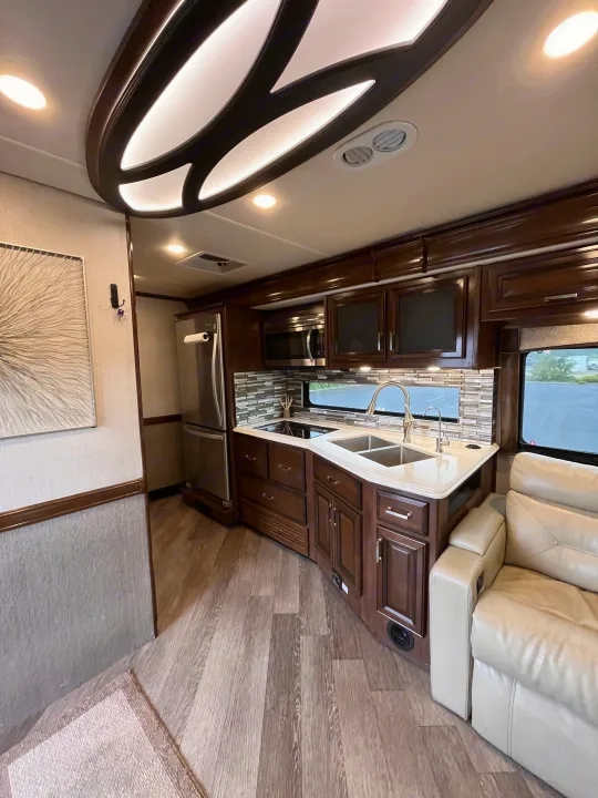 Explore this modern rv rental's kitchen, featuring dark wood cabinetry, stainless appliances, double sink, and comfortable seating.. Fleetwood Pace Arrow 2020
