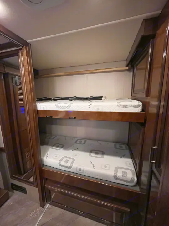 Inside an rv rental: dual bunk beds with "Cool Air" mattresses, framed by warm wooden cabinetry for compact sleeping.. Fleetwood Pace Arrow 2020