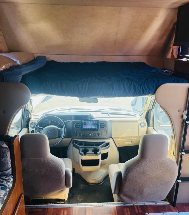 Front cabin of an rv rental, showcasing the driver's area, passenger seats, and a comfortable overhead bed.. Jamboree Sport 2011