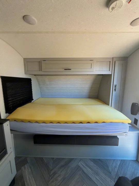 RV rental bedroom features a comfy bed with foam topper, overhead storage, and stylish herringbone flooring.. Forest River Wildwood FSX Plantium 2022