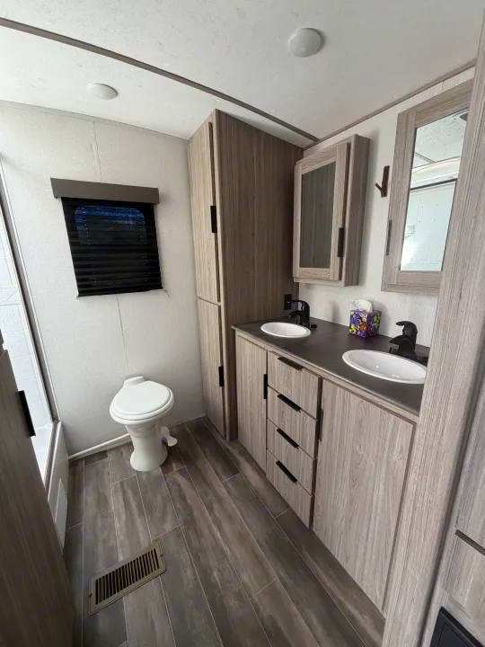 Spacious RV rental bathroom featuring dual sinks, toilet, shower, and modern grey wood cabinetry and flooring.. Keystone RV Passport GT 2021