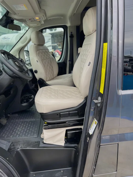 Inside an RV rental: plush beige quilted swivel seats in the front cabin, highlighting comfort and an open door.. Jayco Swift Li 2023